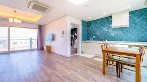 A modern apartment with a large dining area, a kitchen with blue tiles, and a view through the large window.