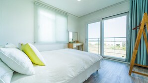 A hotel room with a large bed, a small desk, a mirror, and a view through a sliding glass door. - Jeju Byeoleuldameunbaramarae Pension (Jeju City)