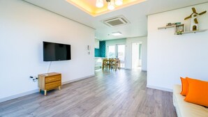 A modern living room with a flat-screen TV, wooden furniture, and a bright orange cushion. - Jeju Byeoleuldameunbaramarae Pension (Jeju City)