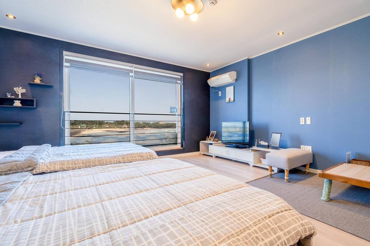 A modern hotel room with two beds, a TV, and a large window offering a view of the outdoors.