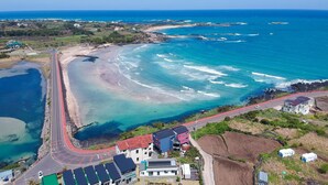Vista aérea de una zona costera con una carretera serpenteando por la playa, edificios con tejados rojos y una vista despejada del océano.