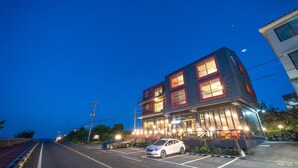 Un edificio de varios pisos con ventanas iluminadas y un estacionamiento al frente.