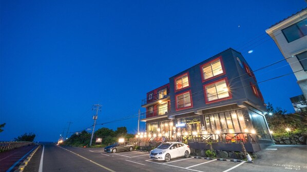 A multi-story building with illuminated windows and a parking lot in front.