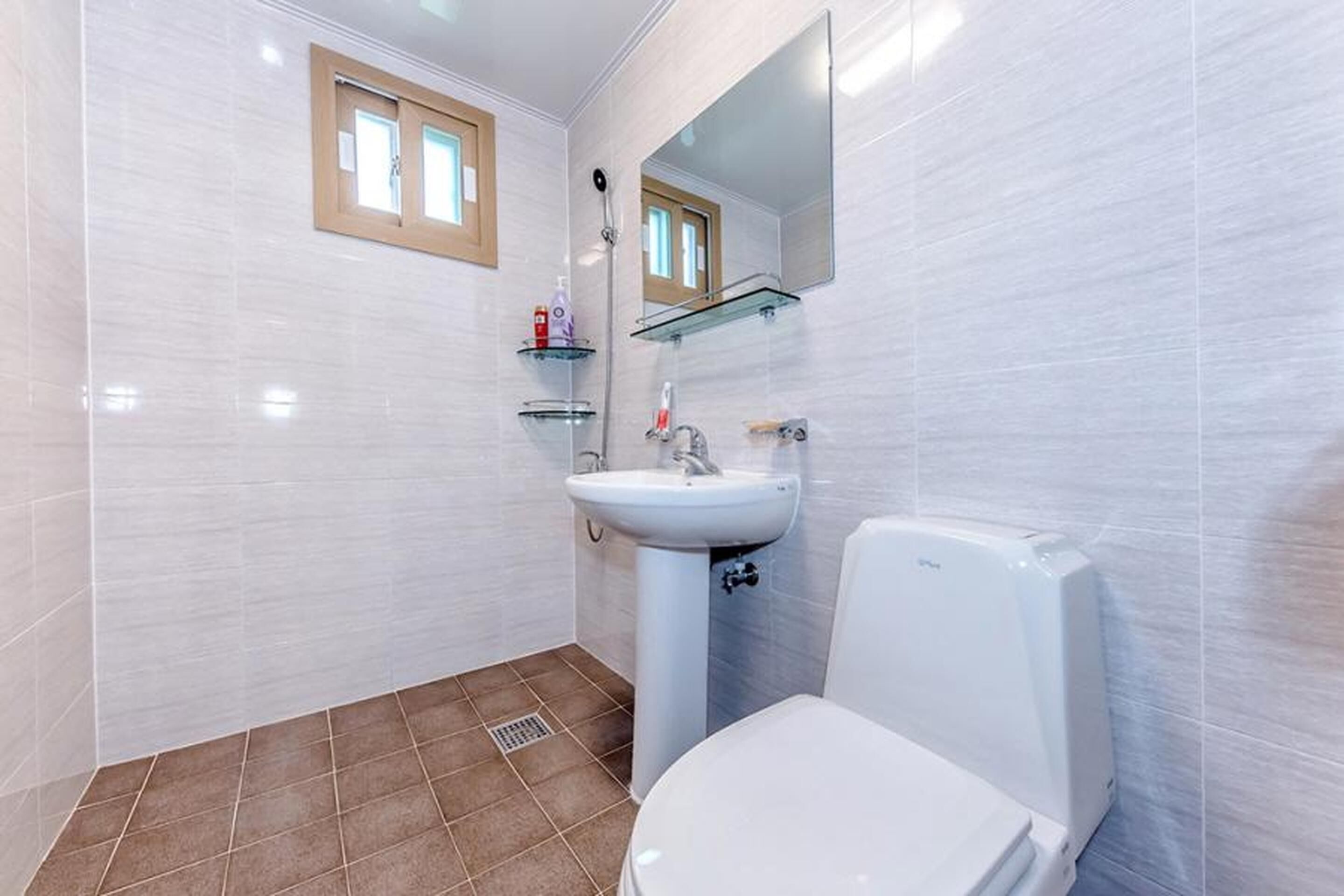 A bathroom with white tiles, a white toilet, a sink with a mirror above it, and a window with a wooden frame.
