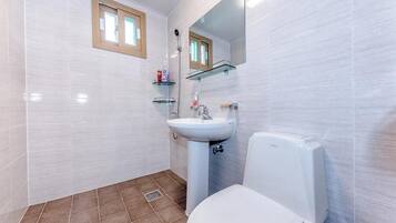 A bathroom with white tiles, a white toilet, a sink with a mirror above it, and a window with a wooden frame.