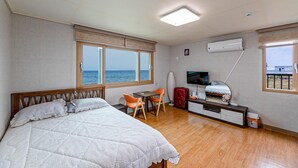 Quarto de hotel com uma cama, uma mesa com uma cadeira, uma televisão e uma janela com vista para o mar.