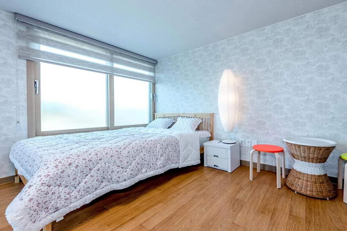 A bedroom with a large bed, a nightstand, a lamp, and two stools.