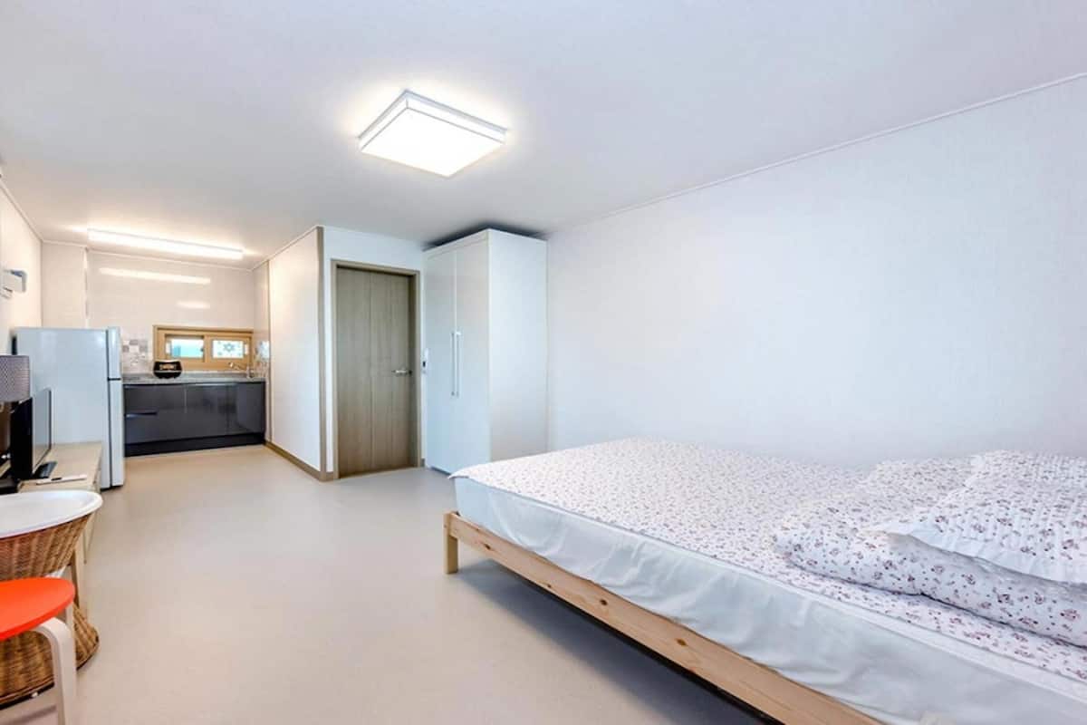 A modern bedroom with a single bed, a small kitchenette, and a bathroom with a toilet and sink.