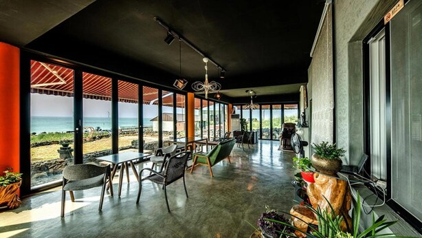 Amplo espaço interno com vista para a praia, incluindo uma mesa de jantar, cadeiras e um espaço de estar também com vista.