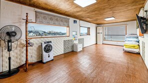 Ein Zimmer mit Holzboden, einem Standventilator, einer mobilen Klimaanlage und einem Fenster mit Blick auf die Stadt.