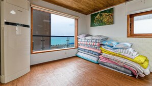 Quarto com uma janela ampla com vista para o mar, um ar condicionado Whisen e uma pilha de roupa de cama dobrada.