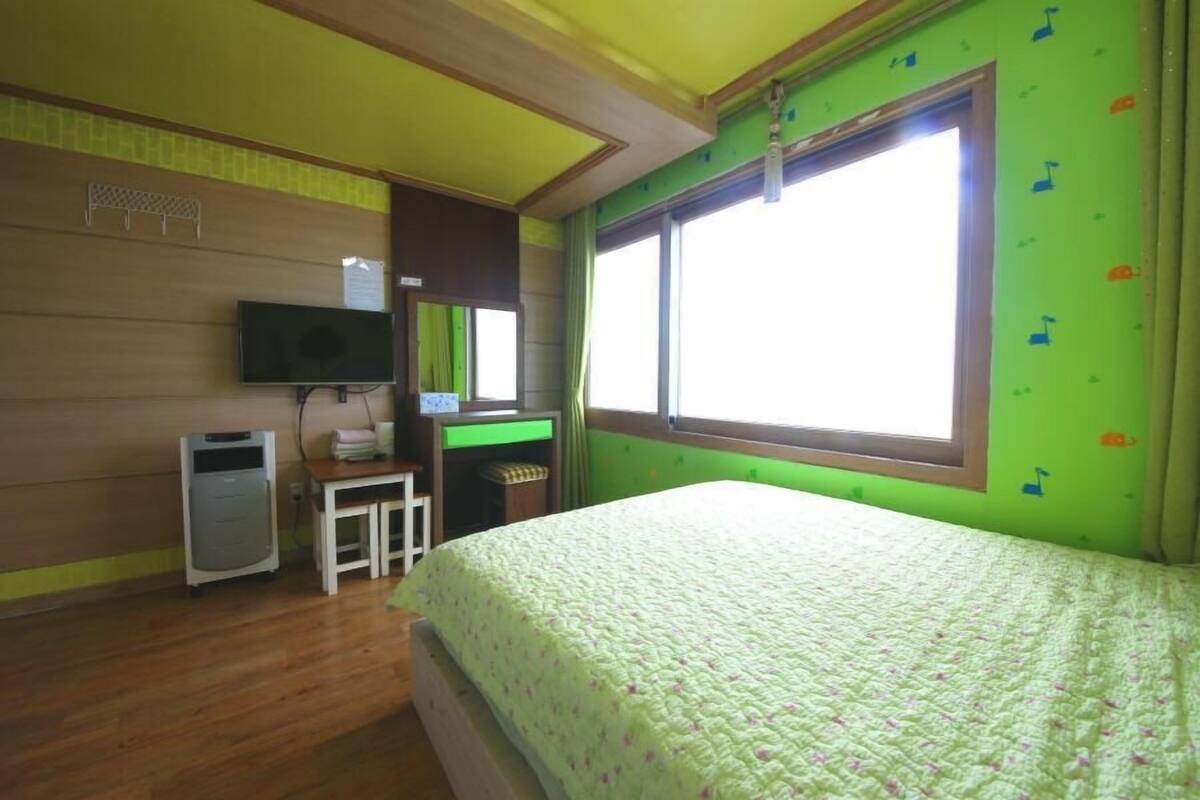 Un dormitorio con cama, escritorio, televisor y ventana.