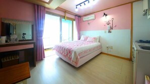 A bedroom with a bed, a desk, a mirror, and a window with curtains. - Jeju Syagaluibada Pension (Jeju City)