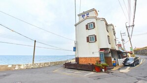 A building with a sign reading "Pension" near the entrance, a parking area, and a view of the sea. - Jeju Syagaluibada Pension (Jeju City)