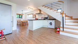Une cuisine moderne dotée d’un îlot central, d’un lave-linge et d’un escalier avec des marches en bois.