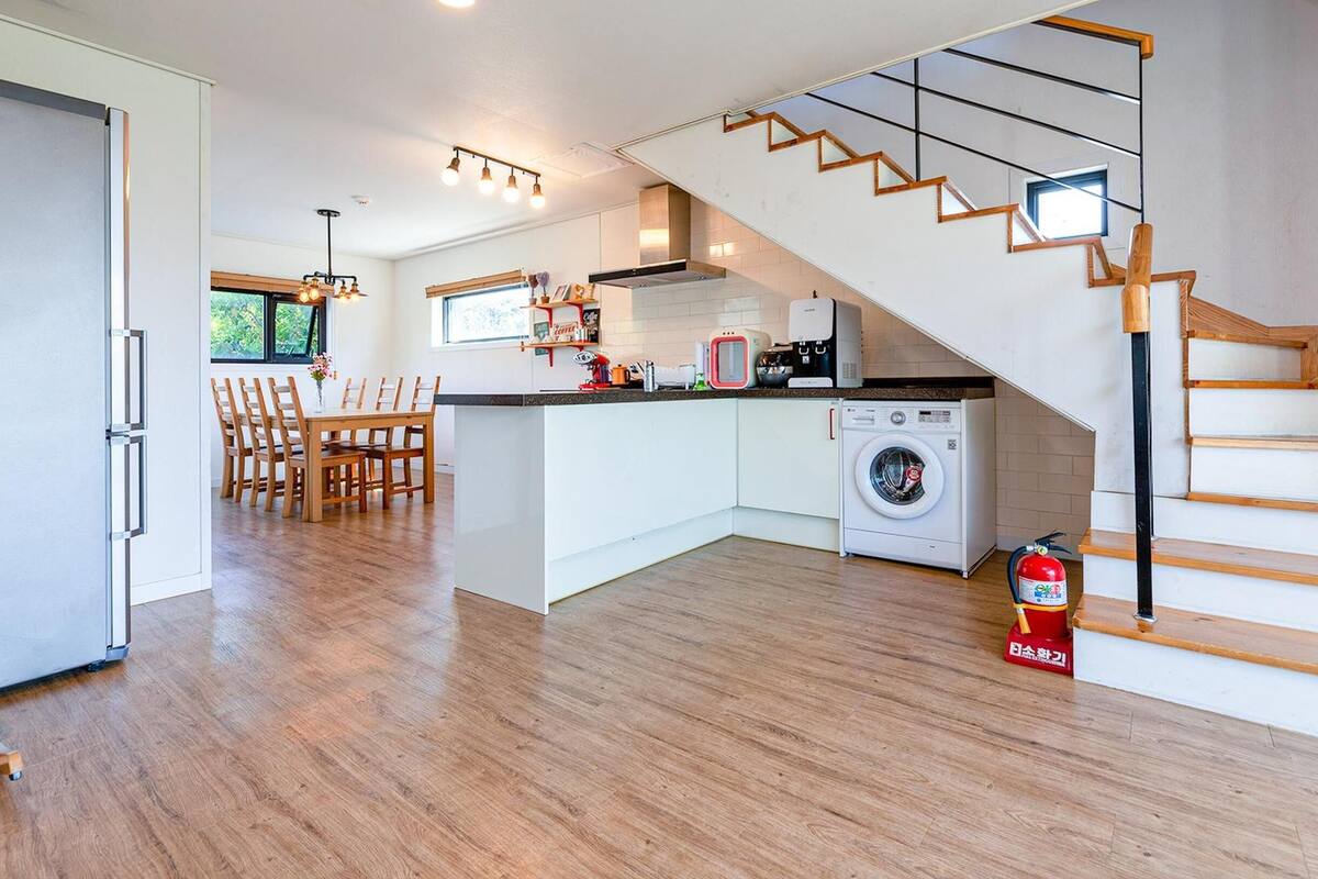 A modern kitchen with a central island, a washing machine, and a staircase with wooden steps.