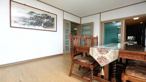 Un coin repas avec une table et des chaises en bois, une œuvre d’art encadrée au mur et une vue sur une autre pièce.