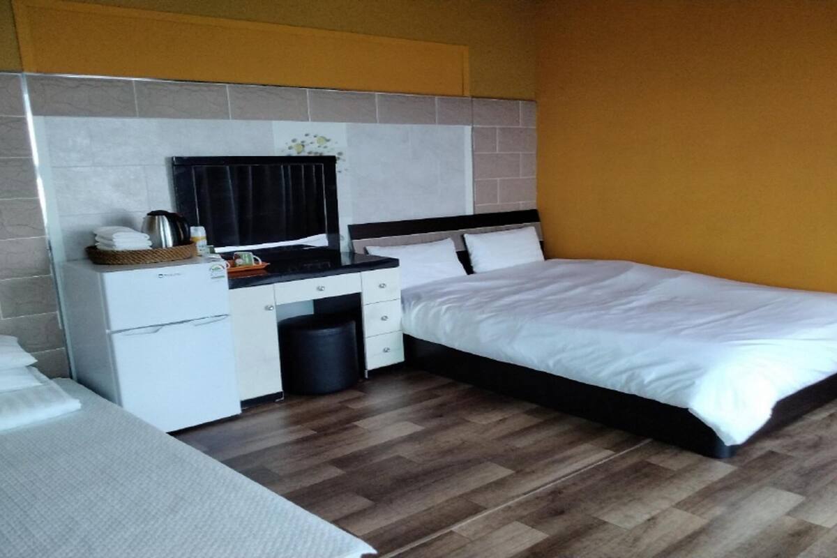 Une chambre d’hôtel avec un lit, un bureau et une chaise, une petite poubelle et une fenêtre.