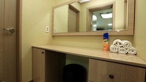 Une chambre d’hôtel équipée d’un bureau en bois, d’un miroir, d’un distributeur de serviettes et d’une poubelle.