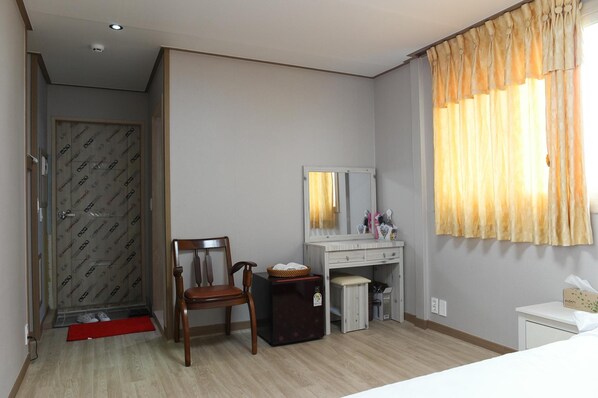 Une chambre d’hôtel avec une chaise en bois, un bureau doté d’un miroir, une petite poubelle et une table de chevet.