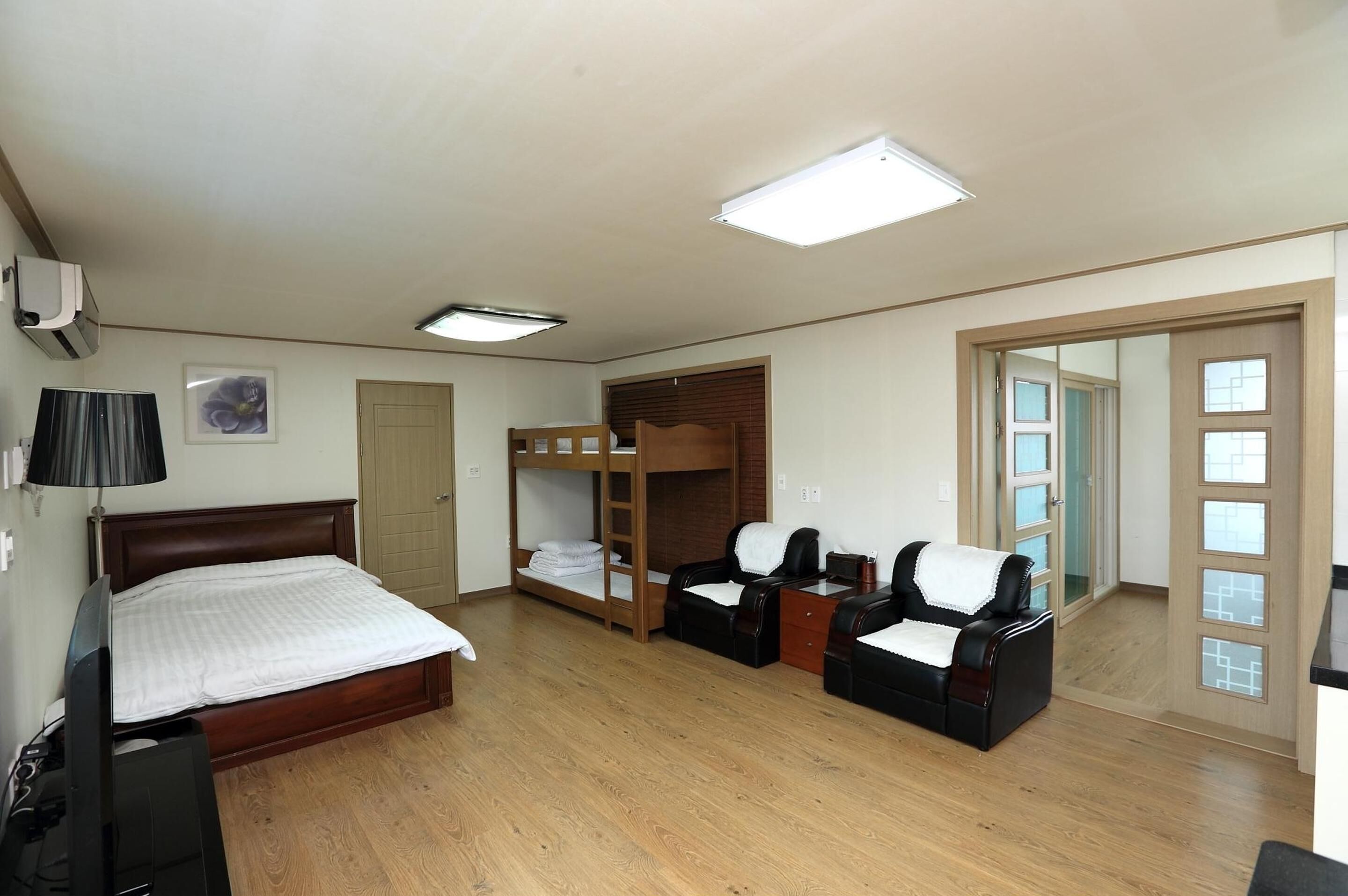 A hotel room with a wooden bed, a bunk bed, two leather chairs, a small table, and a mirror with a view of the outside.