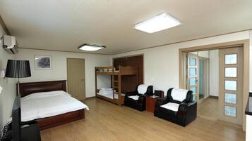 A hotel room with a wooden bed, a bunk bed, two leather chairs, a small table, and a mirror with a view of the outside.