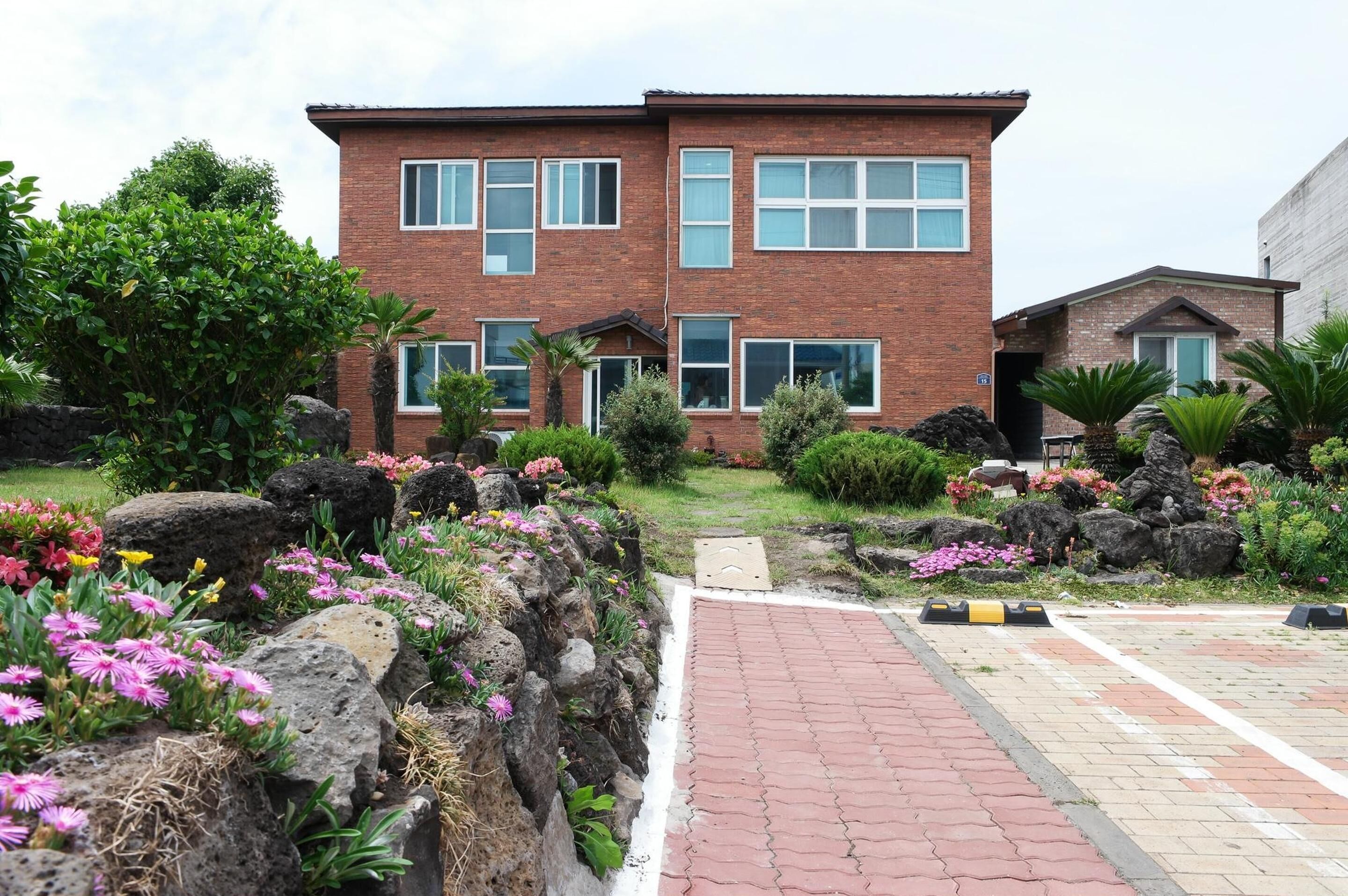 A two-story brick building with multiple windows, surrounded by landscaped gardens with rocks and flowering plants.