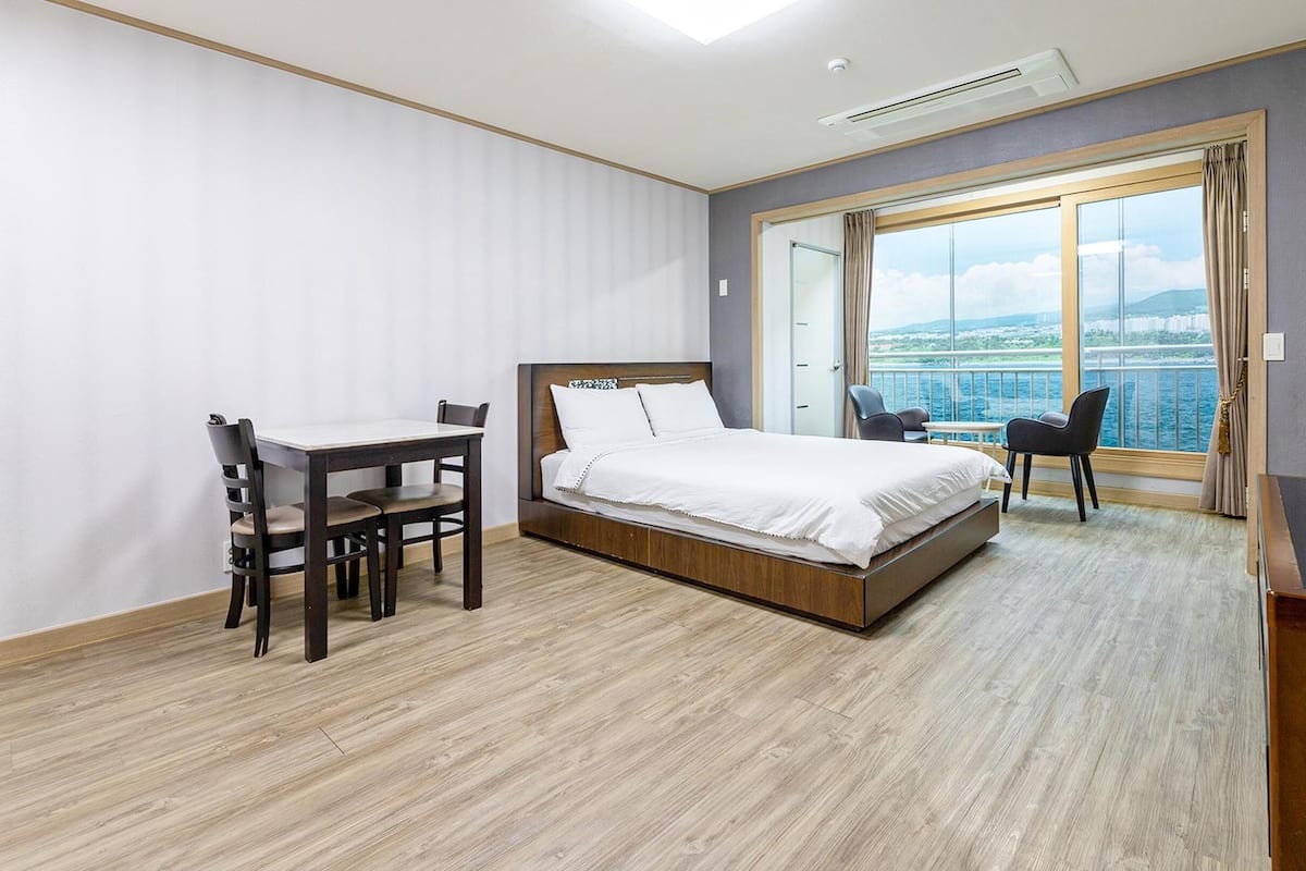 Une chambre d’hôtel avec un lit, un bureau et une chaise, une télévision et un balcon avec vue sur la mer.