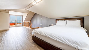A spacious bedroom with a large bed, a balcony with a railing, and a view of the outdoors.