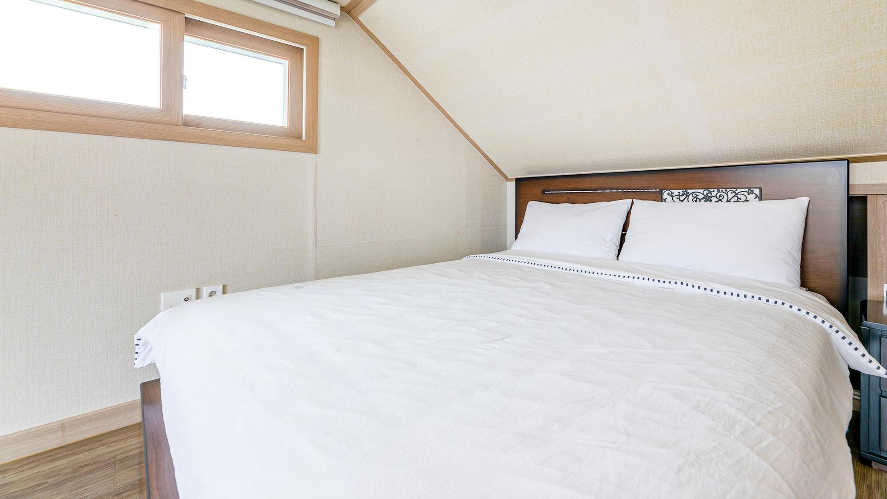 A bedroom with a large bed, a wooden headboard, and a skylight.