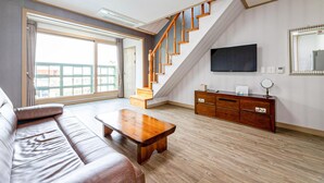 A living room with a wooden staircase, a flat-screen TV, a wooden cabinet, and a large window with a view.