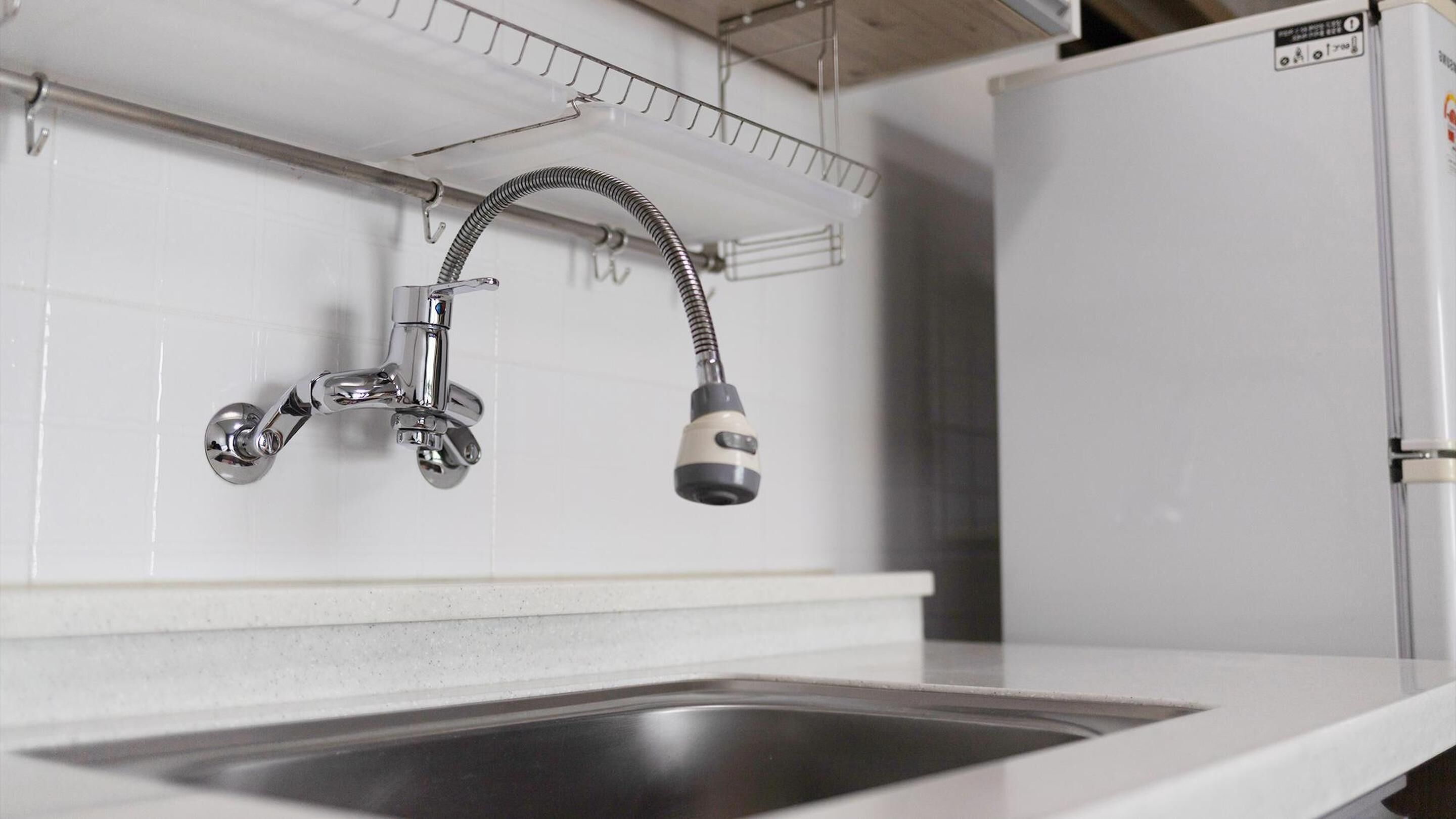 A kitchen with a stainless steel sink, a faucet with a flexible hose, and a white refrigerator.