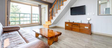 Un salón espacioso con una escalera de madera, un televisor de pantalla plana y un mueble de madera.