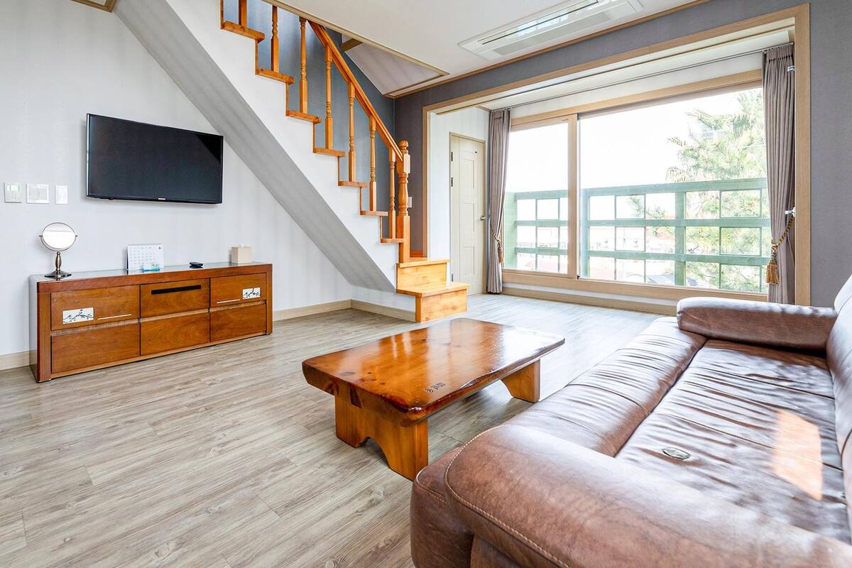Un salon spacieux avec un escalier en bois, un téléviseur à écran plat, une table basse en bois et un canapé en cuir.