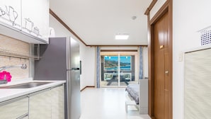 A modern kitchen with a refrigerator, sink, and a view of a balcony with a scenic landscape. - Geoje Rockspa Pension (Geoje)