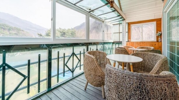 Un espacio de estar al aire libre techado, con muebles de mimbre y vistas a un río y montañas.