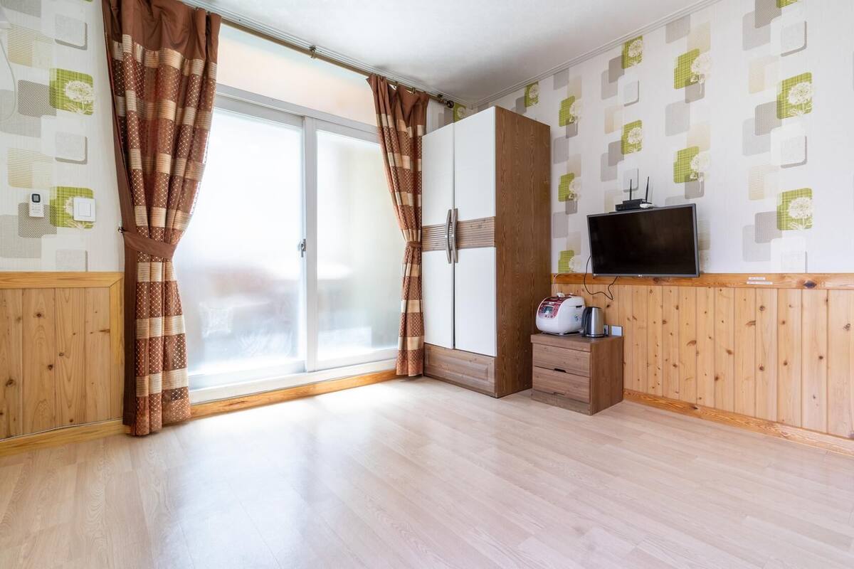 A room with a large sliding glass door, a wardrobe, a television, and a small wooden cabinet.