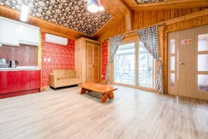 Una habitación acogedora con techo de madera, un sofá, un banco de madera y una zona de cocina con armarios rojos y una estufa.