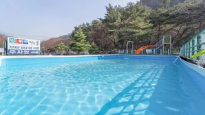 Una piscina azul cristalina con un tobogán, rodeada de árboles y una montaña al fondo.