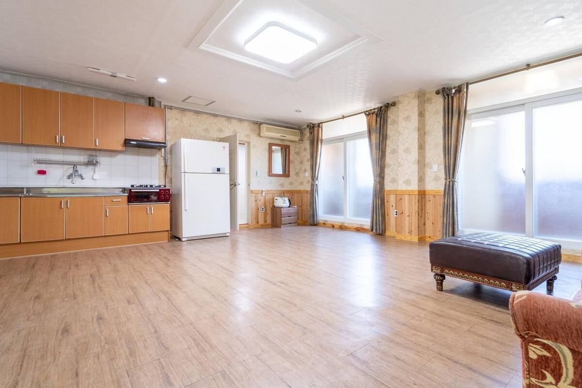 A spacious living area with a kitchen, a sofa, and a large window providing natural light.