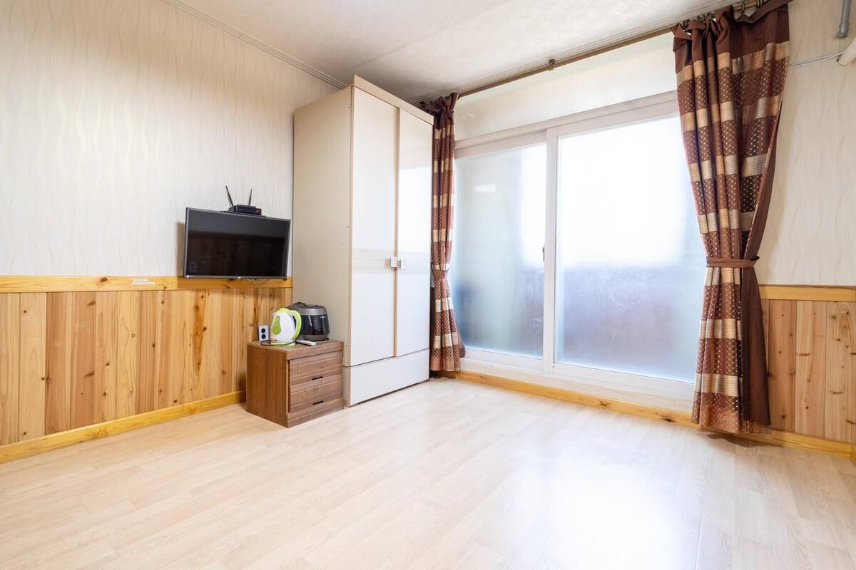 A room with wooden paneling, a sliding door, a television, a small wooden cabinet, and a window with patterned curtains.