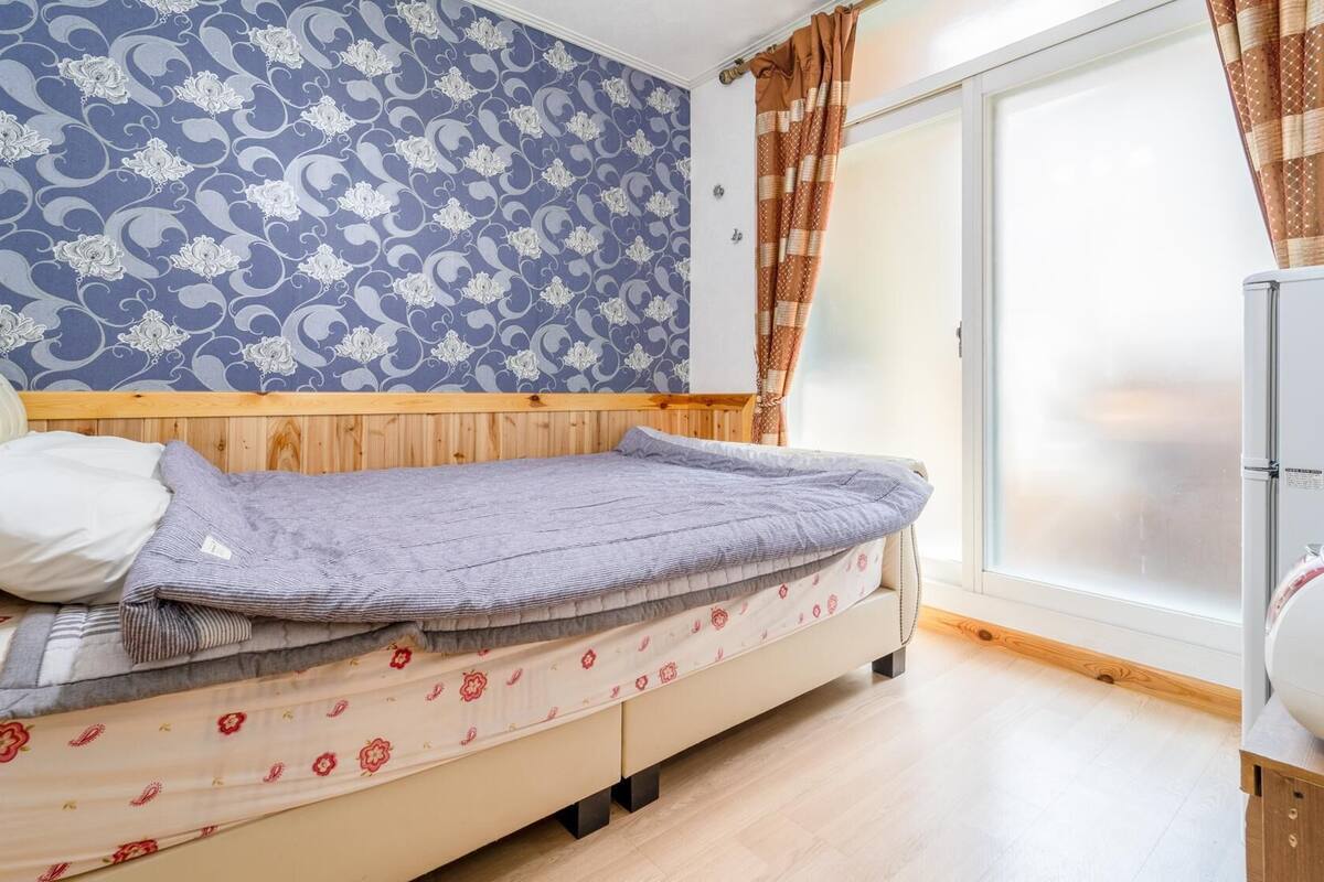 A bedroom with a bed, a wardrobe, a window with curtains, and a patterned wall.