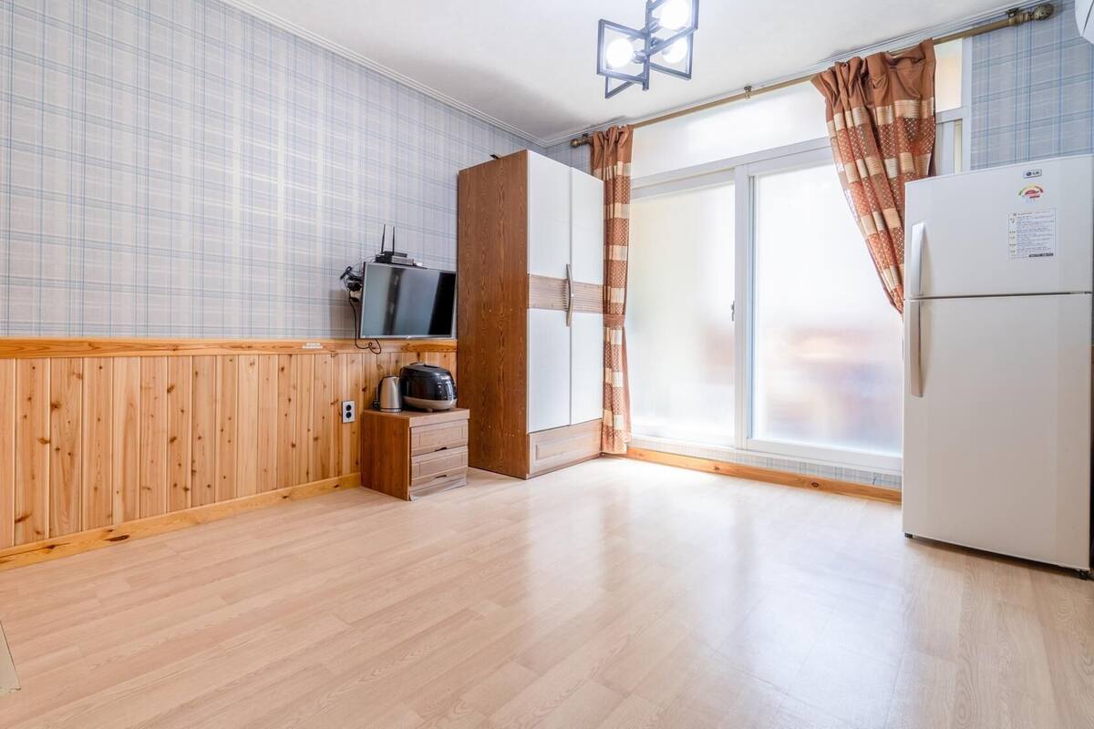 A small, clean kitchen with wooden paneling, a refrigerator, a microwave, and a television.