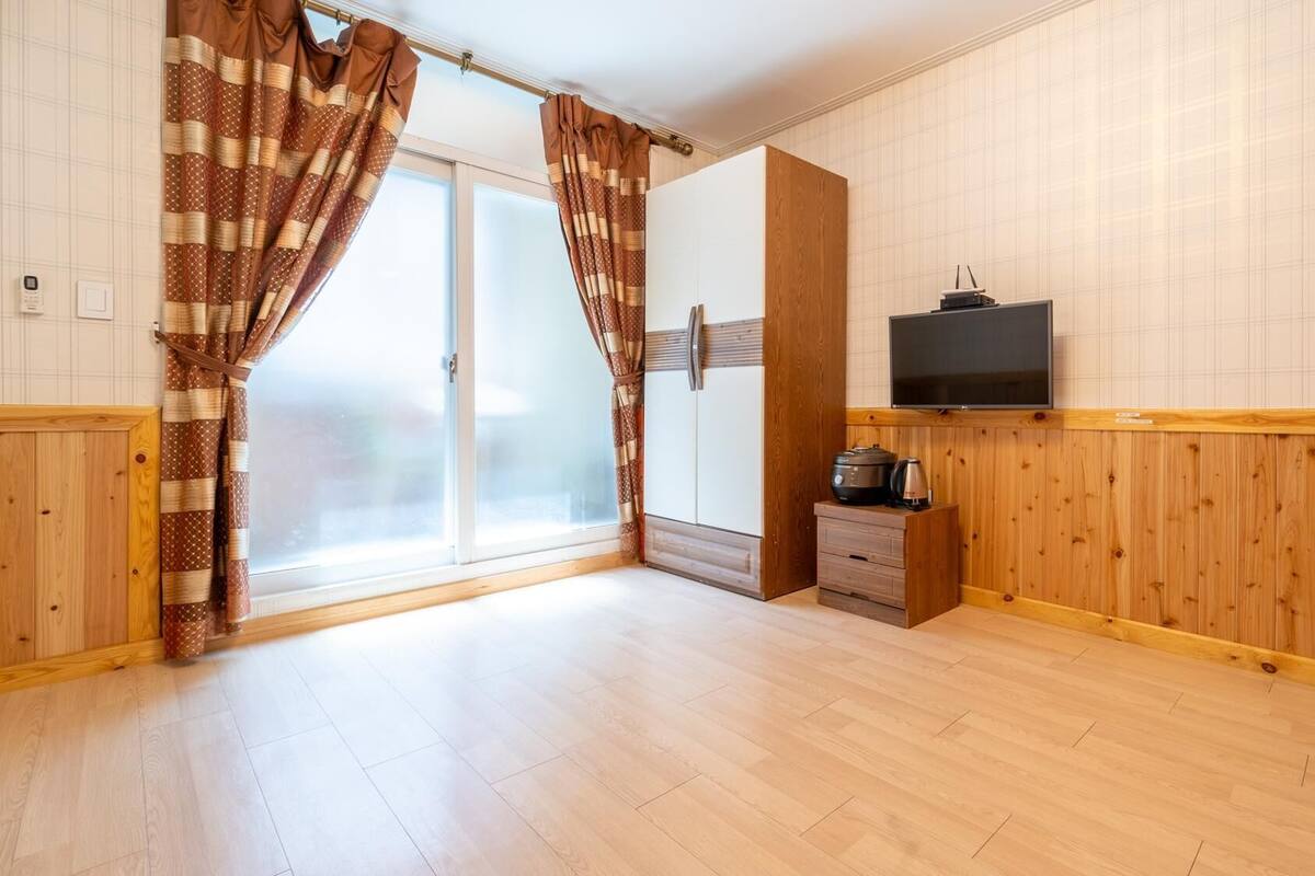 A room with wooden paneling, a sliding glass door, a flat-screen TV, and a small kitchenette with a stove and kettle.
