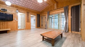 Una habitación amplia con suelos de madera, una gran mesa de madera, televisión y un balcón con cortinas.