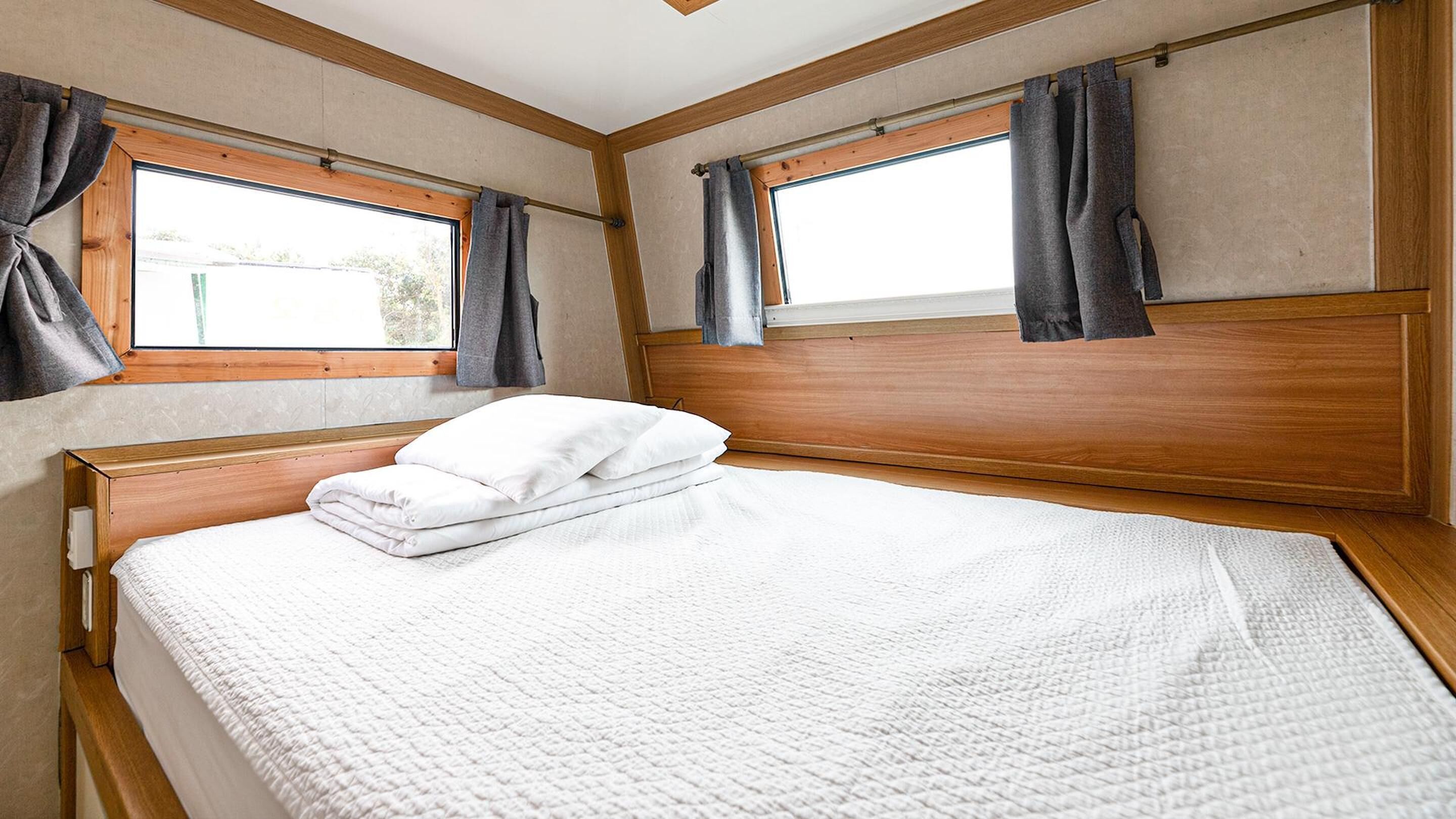 A neatly made bed with white bedding and pillows, wooden headboard, and curtains on windows.