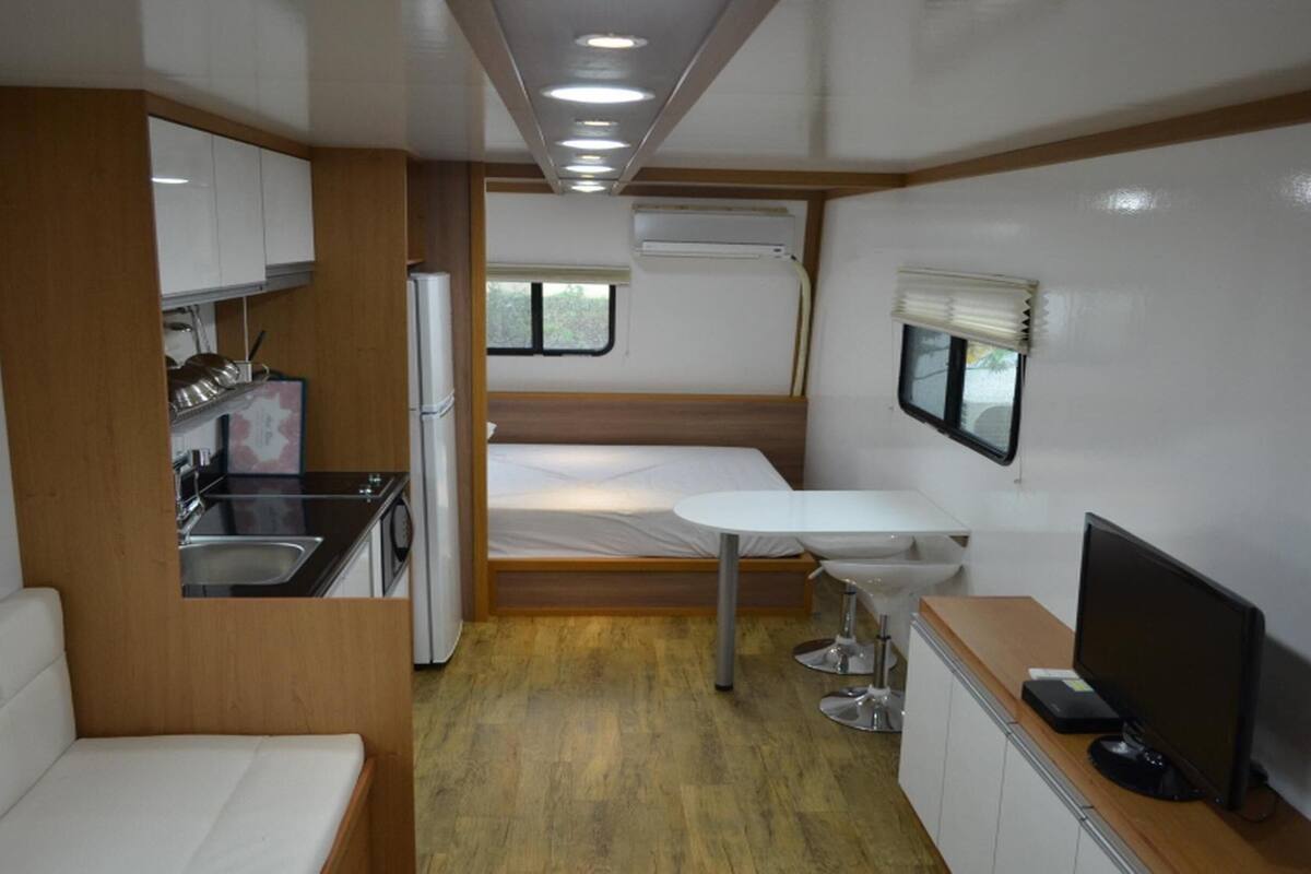 A compact RV interior with a kitchenette, a bed, a small dining table, and a TV.