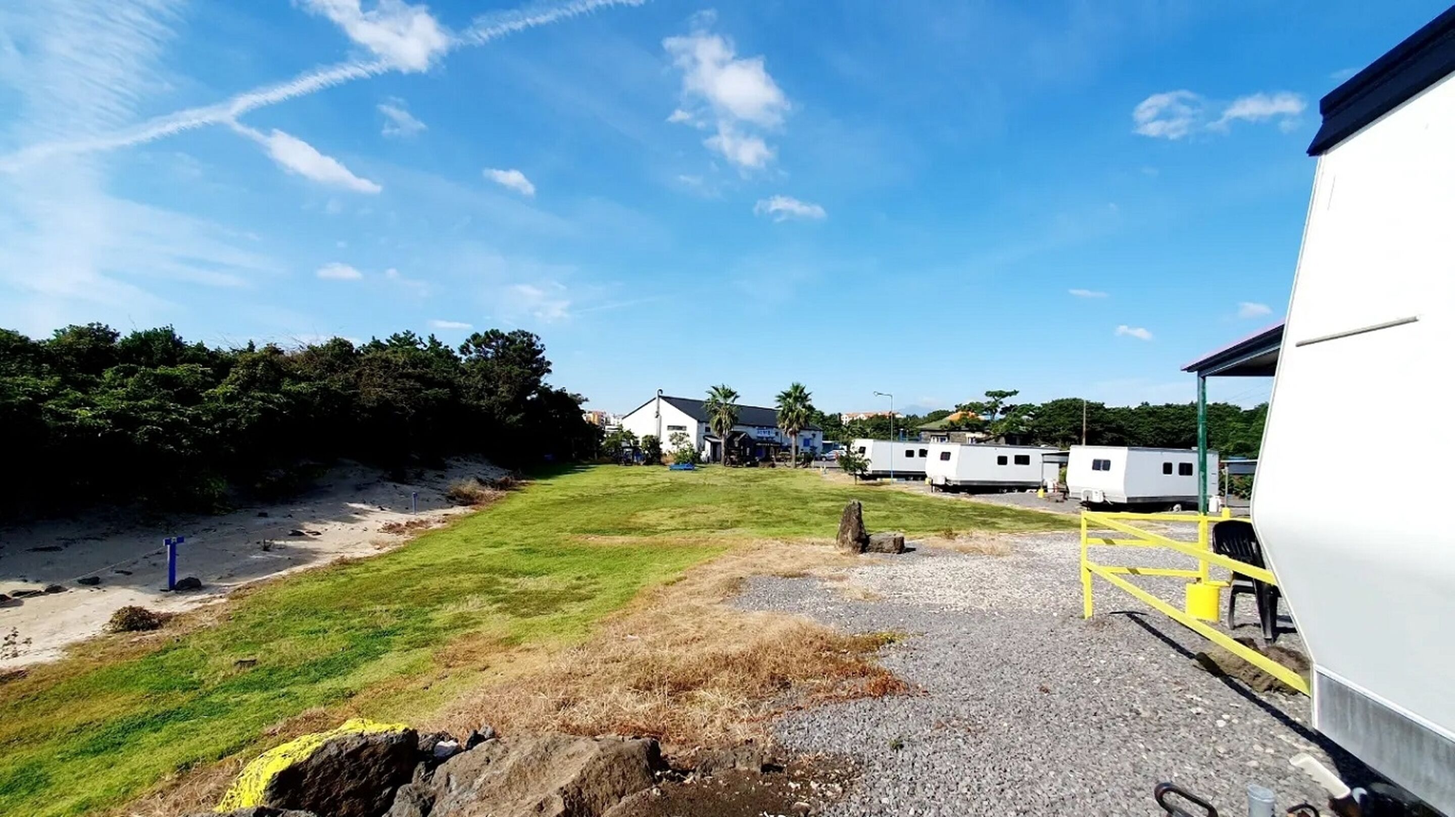 Un camping con vehículos recreativos, una zona con césped y un edificio al fondo.
