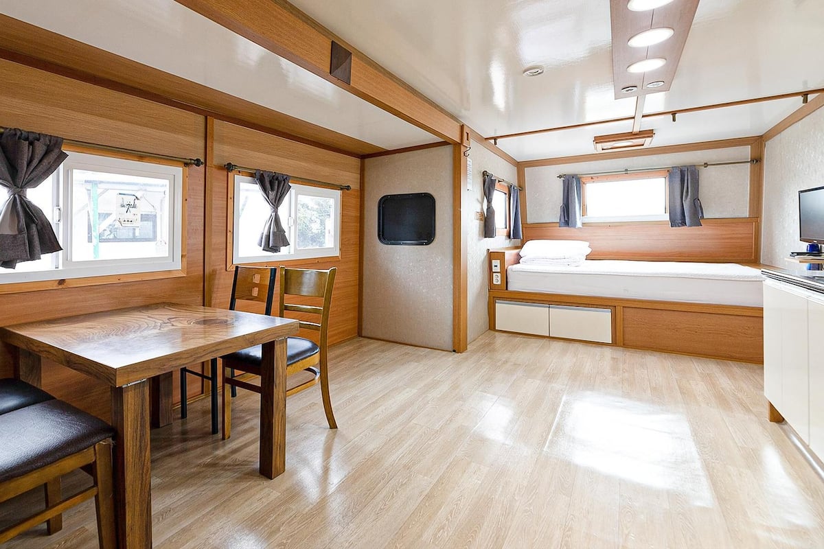 A compact RV interior with a dining area, a bed, and a small kitchenette.