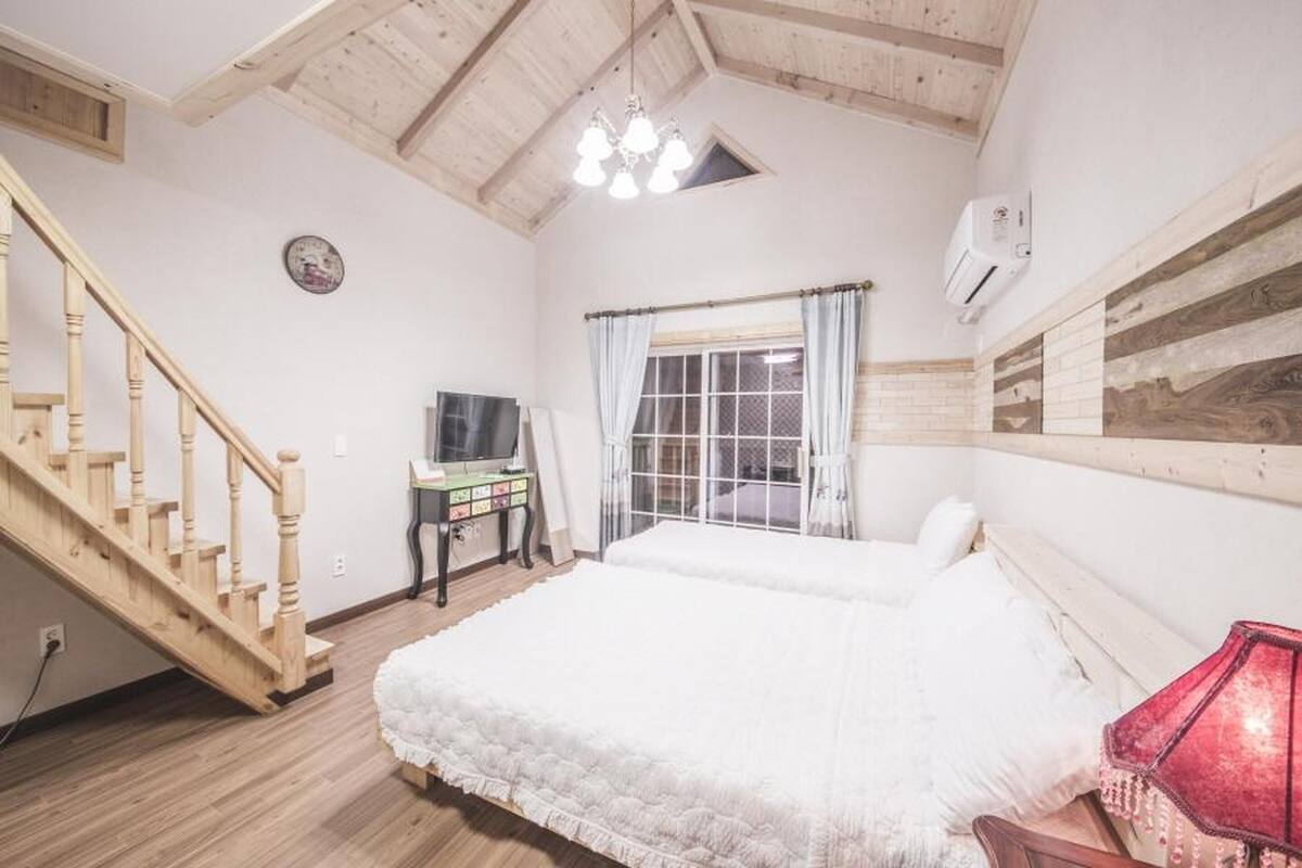 A bedroom with a wooden staircase, a bed, a desk with a computer, and a window with curtains.
